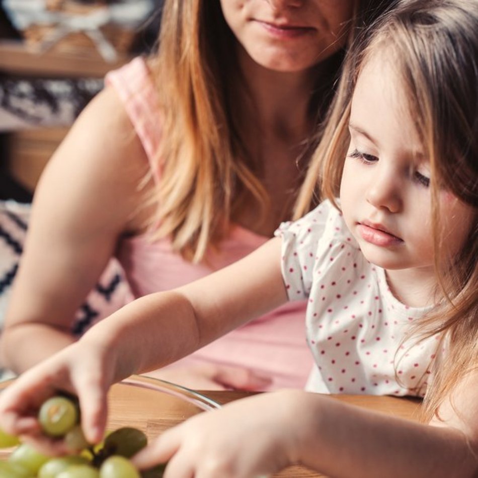 Gesunde Zwischenmahlzeit – Kind beim Snacken von Trauben Mädchen greift nach Trauben in einer Schale